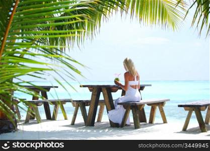 woman sitting in a tropical cafe on the background of a palm trees and sky and sea