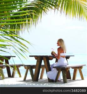 woman sitting in a tropical cafe on the background of a palm trees and sky and sea