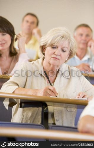 Woman sitting in adult classroom taking notes with students in background (selective focus)