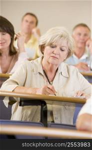 Woman sitting in adult classroom taking notes with students in background (selective focus)