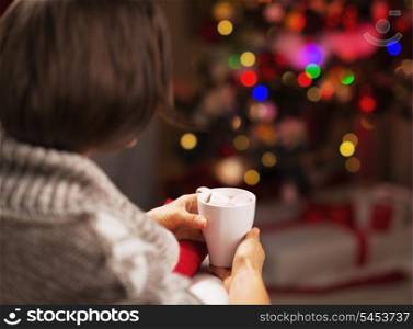 Woman sitting in armchair with cup of hot chocolate in front of christmas tree . rear view