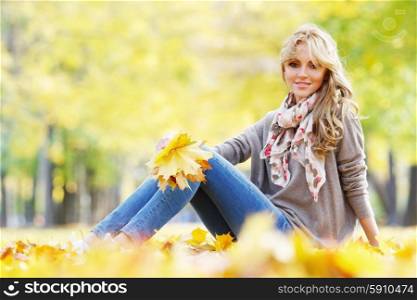 Woman sitting in autumn park. Beautiful young woman sitting and holding bunch of fall leaves in autumn park
