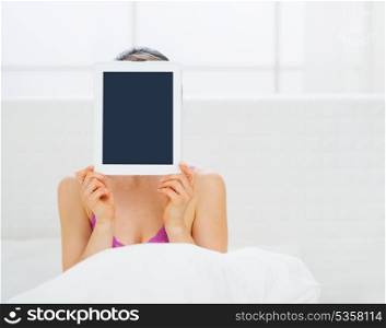 Woman sitting in bed and hiding tablet PC in front of face