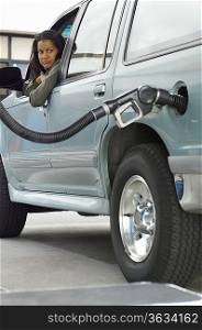 Woman sitting in car looking at fuel pump