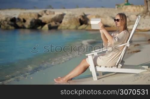 Woman sitting in chaise longue near the sea and taking pictures using tablet computer