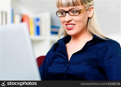 Woman sitting in front of a bookshelf, working with a laptop in the internet from home, she is a telecommuter