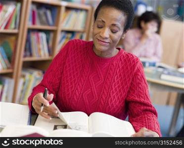 Woman sitting in library with a book and notepad (selective focus)