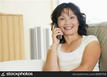 Woman sitting in living room using telephone and smiling