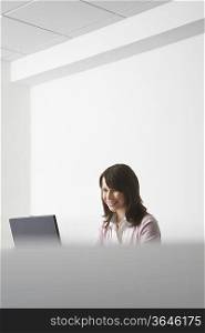 Woman sitting in office, using laptop and smiling