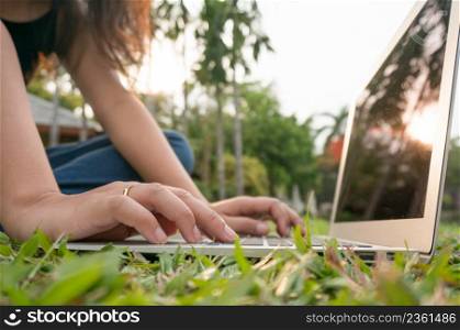 Woman sitting in park on the green grass with laptop, student studying outdoors. Copy space