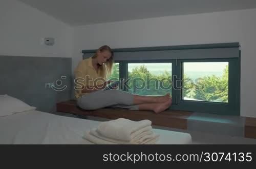 Woman sitting in room on window-sill and using tablet
