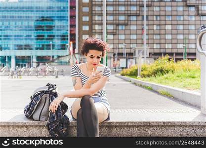 Woman sitting in urban area texting on smartphone, Milan, Italy