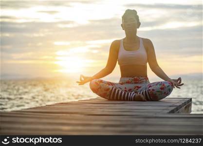 woman sitting in yoga meditating pose at sea side against beautiful sun rising sky