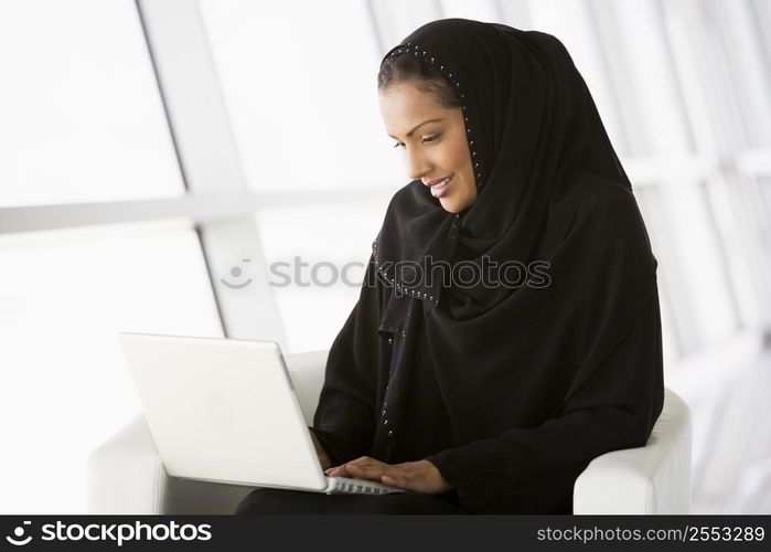 Woman sitting indoors with laptop smiling (high key/selective focus)