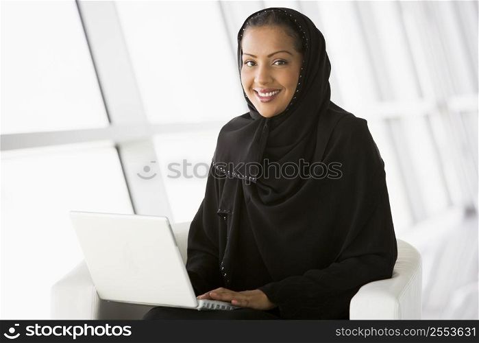 Woman sitting indoors with laptop smiling (high key/selective focus)