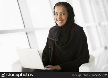 Woman sitting indoors with laptop smiling (high key/selective focus)