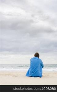 Woman sitting on a beach beneath a wide cloudy sky covered with a blue towel