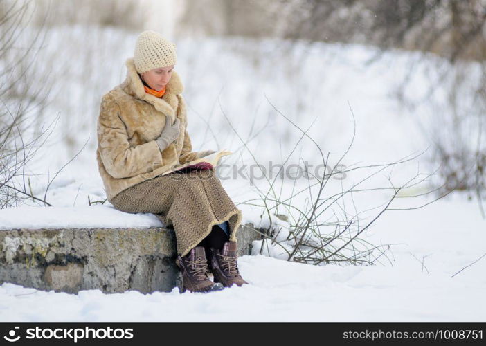 Woman sitting on a bench and reading a book in winter. Snow.