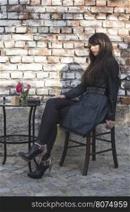 Woman sitting on a chair in coffee shop. Vintage brick wall background