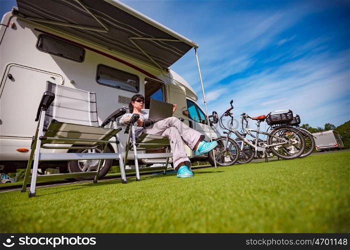 Woman sitting on a chair near the camper and looking at a laptop. Caravan car Vacation. Family vacation travel, holiday trip in motorhome