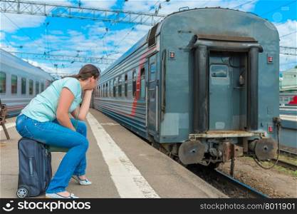 woman sitting on a suitcase and looking at the departing train