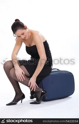Woman sitting on a suitcase rubbing her ankle