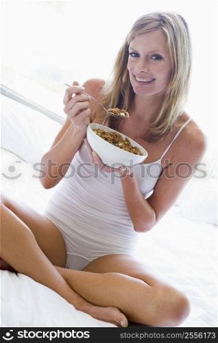 Woman sitting on bed eating cereal smiling