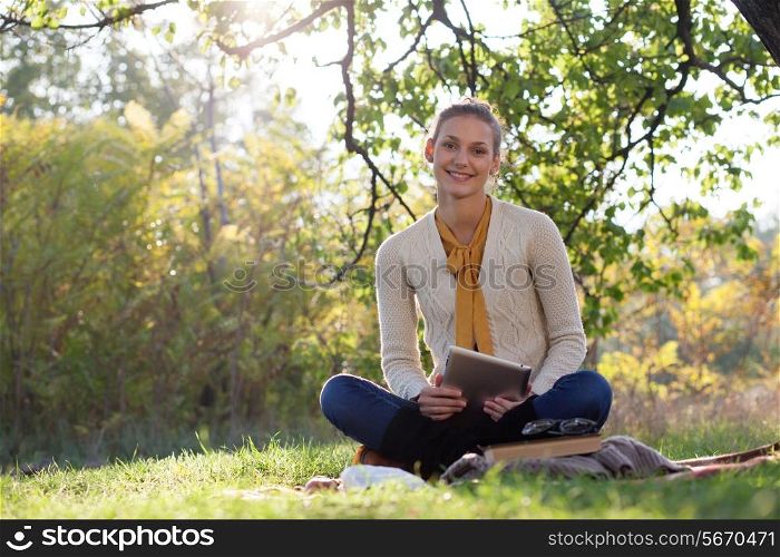 woman sitting on bedding on green grass with tablet pc during picknic in the park