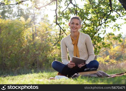 woman sitting on bedding on green grass with tablet pc during picknic in the park