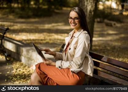 Woman sitting on bench in park during autumn weather using tablet pc and  checking social media.