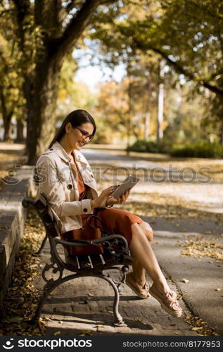 Woman sitting on bench in park during autumn weather using tablet pc and  checking social media.