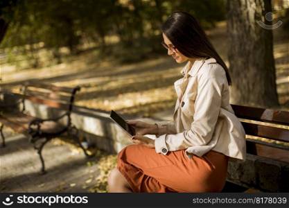 Woman sitting on bench in park during autumn weather using tablet pc and  checking social media.