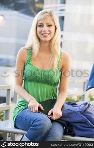 Woman sitting on bench outdoors with notebook smiling (selective focus)
