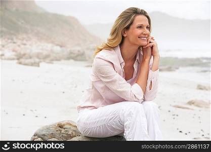 Woman sitting on boulder on beach smiling