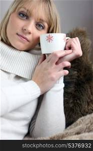 Woman sitting on cosy sofa with mug of coffee