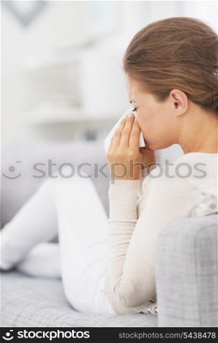 Woman sitting on couch and blowing nose into handkerchief