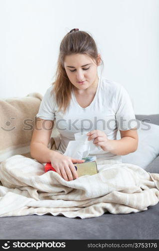 Woman sitting on couch covered in blanket and pulling tissues