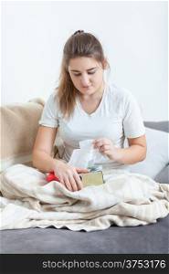 Woman sitting on couch covered in blanket and pulling tissues