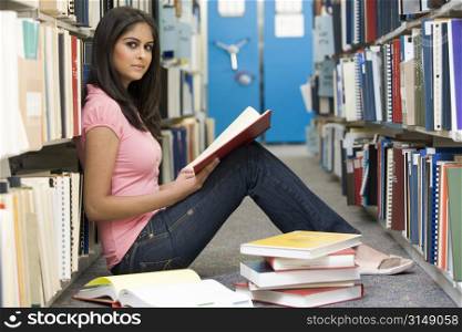 Woman sitting on floor in library holding book