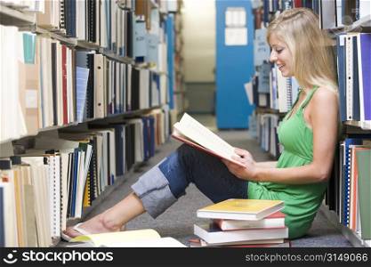 Woman sitting on floor in library reading book