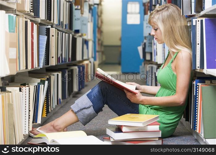 Woman sitting on floor in library reading book