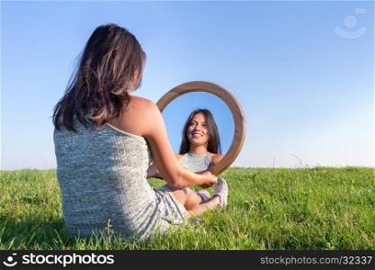 Woman sitting on grass looking at her mirror image