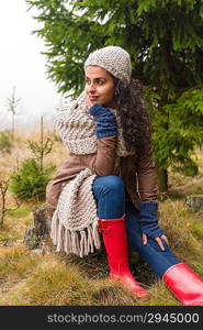 Woman sitting on ground autumn foggy pinewood in knitted scarf