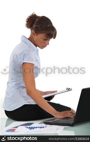 Woman sitting on her desk with a clipboard and laptop