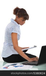 Woman sitting on her desk with a clipboard and laptop