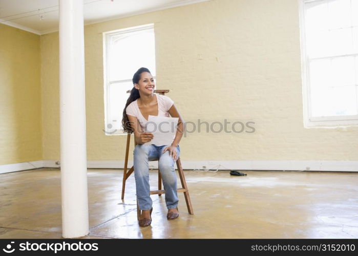 Woman sitting on ladder in empty space holding paper