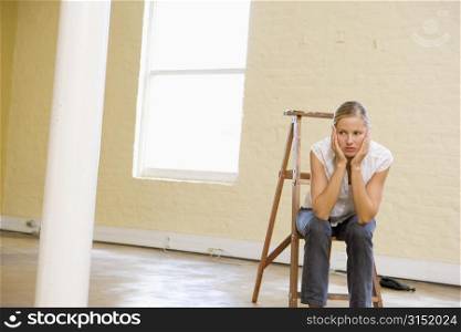Woman sitting on ladder in empty space looking bored