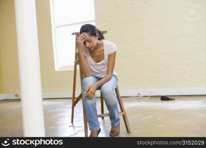 Woman sitting on ladder in empty space looking tired