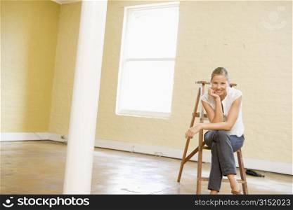 Woman sitting on ladder in empty space smiling