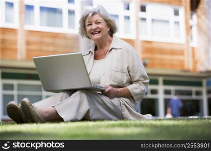 Woman sitting on lawn of school with laptop